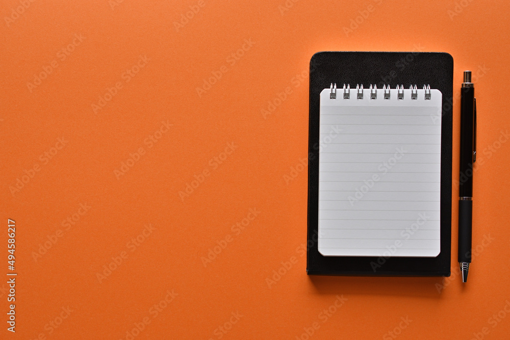 Aufkleber a notebook and pen in a simple composition on orange background. copy space available.