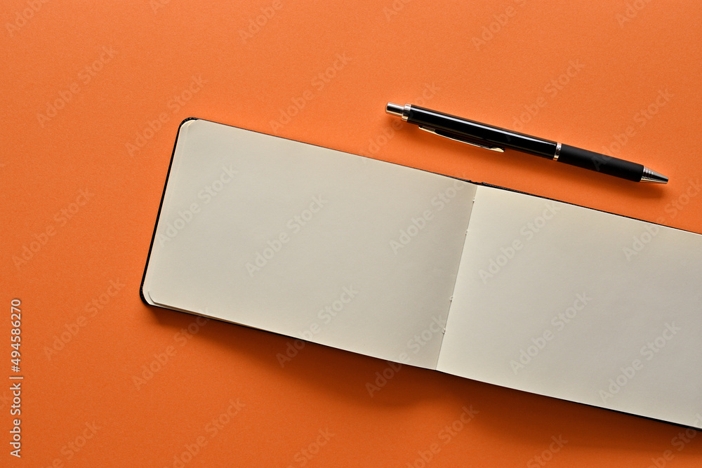 Poster a notebook and pen in a simple composition on orange background. copy space available.