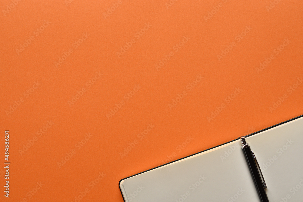 Poster a notebook and pen in a simple composition on orange background. copy space available.