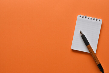 A notebook and pen in a simple composition on orange background. Copy space available.