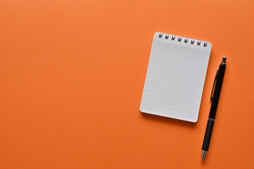 A notebook and pen in a simple composition on orange background. Copy space available.