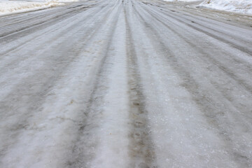 A low angle view of an ice covered road.The road is completely covered with ice, and the ice has grooves worn in it by passing traffic.
