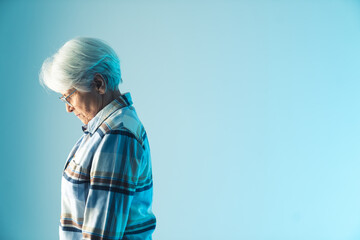 resigned elderly gray-haired grandmother lowering her head in disappointment, side view medium studio shot with blue background. High quality photo