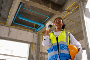 A black female engineer working at a construction site, she wears a hard hat,a safety helmet, and a reflective vest. In her hand was a radio.
African woman working happily ,
looking at camera.