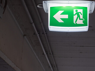 An illuminated emergency exit sign hangs on the ceiling of a parking garage. 
