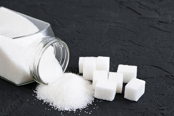 Glass jar with sugar black background.Diabetes. Scattered white sugar on a black table. Copy space. Place for text.Extra calories