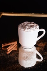 white cup with creamy drink and cinnamon isolated on black background