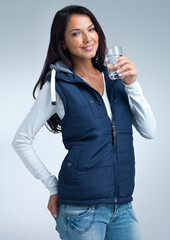 Got to keep it healthy this winter. Young woman drinking water - isolated on gray.