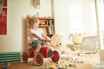 Imaginative play is essential to a childs development. Shot of a little boy playing on a toy car at home.