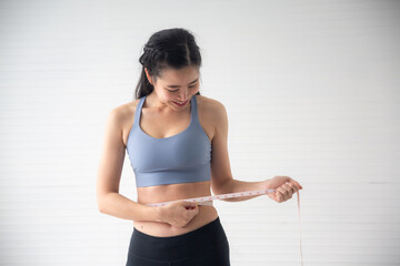 Fototapeta na wymiar young Asian woman measure a body proportions, health fitness to slim body and diet concept, female person using tape with her body care to checking a shape size