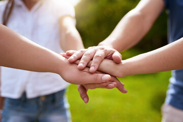 Whos the best family in the world. Closeup of a group of people forming a huddle with their hands while standing outside in a park during the day.
