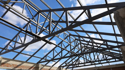 Steel roof structure for building construction. Metal roof structure of a building under construction on a blue sky background with white clouds. Selective focus