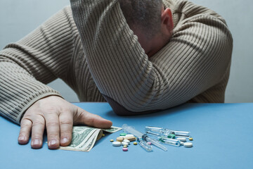 The man hides his face with one hand, holds money in the other, and medical preparations are in...