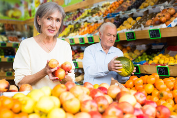 Obraz premium European old man and woman choosing fresh fruits in greengrocer.