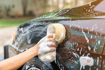 Woman hand hold sponge cleaning car at home.