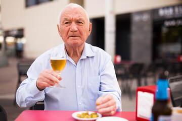 Old European man sitting at table on restaurant terrace and drinking beer.