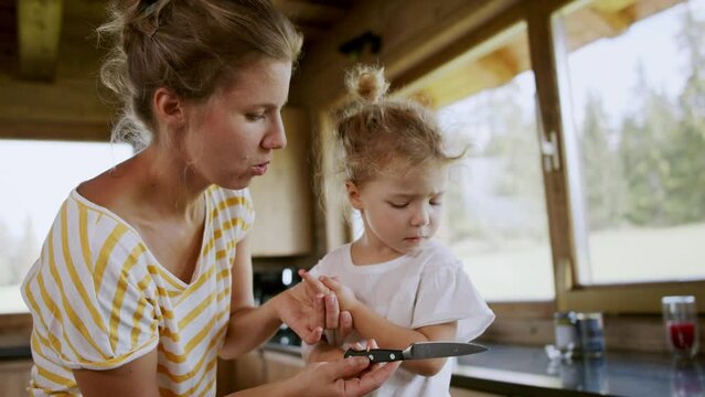 Mother blowing her little daughter's bleeding finger cut with knife at home.