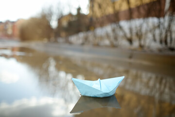 Color origami paper boat in large puddle on street near town houses. Paper ship floating in water. Activities for kids in early spring