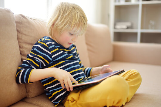 Preschooler boy learning on distance by digital tablet or playing computer game sitting on couch at home. Little child watching cartoon or movie. Homeschooling, online education.