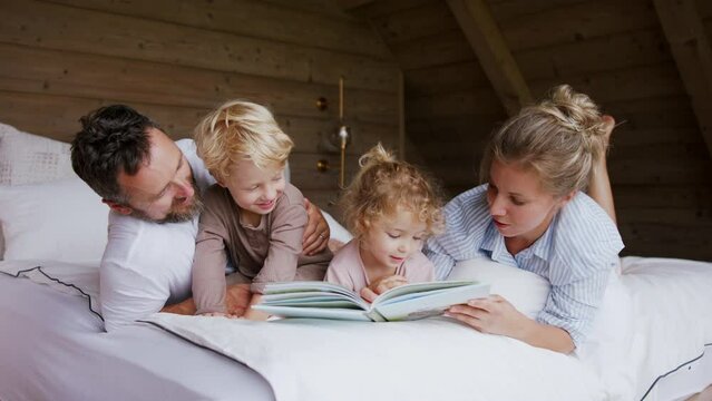 Happy young family with small children having fun in bed when reading book.