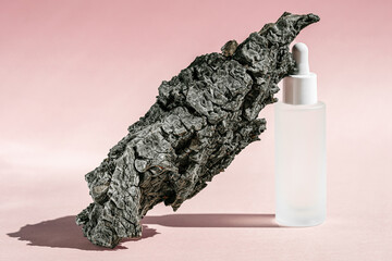 Serum cosmetic bottle mockup with bark tree on pink background, shadow from sun, natural light from...