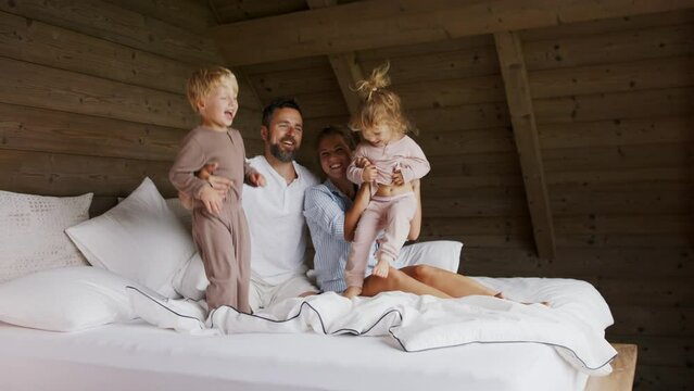 Happy young family with small children having fun in bed on holiday.