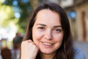 Closeup portrait of cheerful brunette outdoors on blurred summer city street background