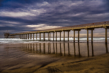 2022-03-23 SCRIPPS PIER WITH NICE WAVES CRASHING A REFLECTION IN THE WATER AND A DARK STORMY CLOUDS NEAR LA JOLLA CALIFORNIA-