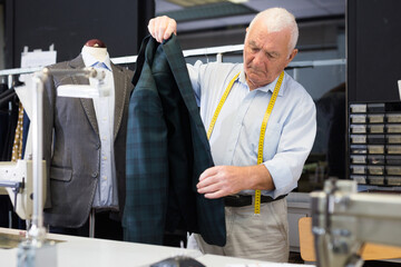 Professional tailor inspects mens jacket before starting work in the workshop