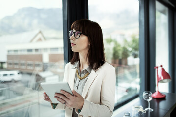 She always makes informed business decisions. Shot of a young businesswoman using a digital tablet while standing near a window in an office.