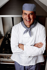 Senior chef with hands folded standing in front of vent hood. Portrait of a cheerful senior chef...