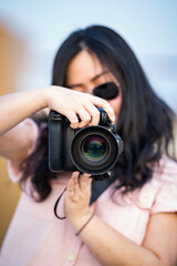 Amateur sunglasses Asian Woman take a photo with professional mirrorless camera at outdoor blue rooftop building in twilight time.