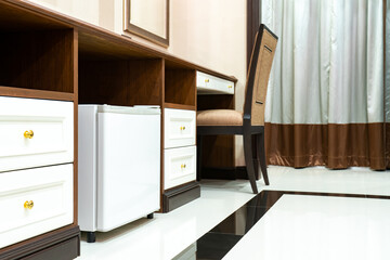 Refrigerator fridge mini size under the table counter with wooden desk beside it in hotel delux room. - obrazy, fototapety, plakaty