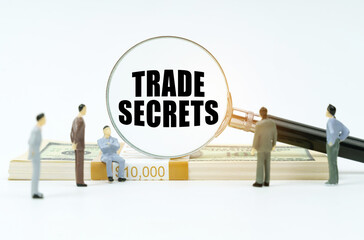 Fototapeta premium On a white surface, a dollar, figurines of people and a magnifying glass with the inscription - TRADE SECRETS
