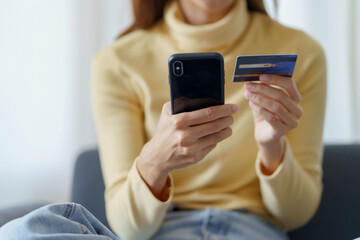 Young woman using smartphone and credit card for online shopping at home.