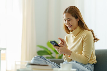 Young Asian woman using smartphone to send text , work or play social media at home.