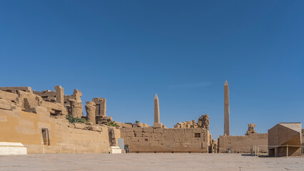 Paved square, dilapidated walls of the ancient Karnak temple in Luxor. Two tall obelisks against a clear blue sky. Copy space. Egypt