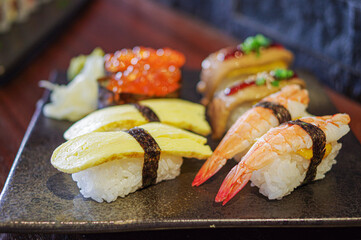 Tamago egg nigiri, shrimp nori nigiris, Ikura salmon roe sushi foie gras on black plate