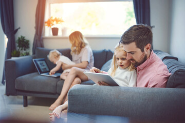 They keep their home connected. Shot of an adorable little girl using a digital tablet with her father on the sofa at home.
