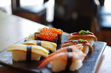Ikura salmon roe sushi and grilled beef tongue, foie gras, tamago egg, shrimp nori nigiri on black plate