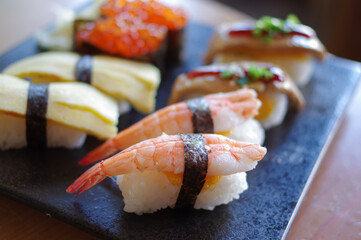 nigiri sushi with shrimp prawn nori tamago egg salmon roe foie gras scallion on black plate close up view