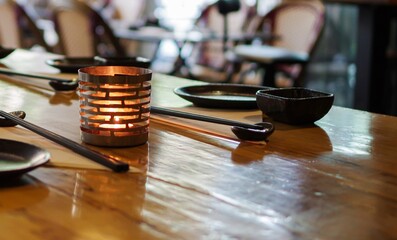 metal candle holder and black chopsticks on wooden table at japanese restaurant