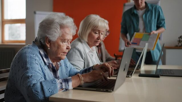 Senior group in retirement home with young instructor learning together in computer class