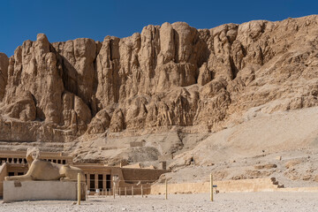 Funeral temple of Pharaoh's Queen Hatshepsut in Luxor. Colonnades, terraces, a damaged sculpture of the sphinx are visible. A picturesque cliff with steep slopes against the blue sky. Egypt