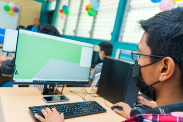 Dark-skinned Central American student in technical education glasses uses a desktop computer to do...