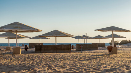 Morning on the Red Sea coast. On the beach there are wicker fences and lattice umbrellas from the sun. There are no people. Light and shadows on the undulating sand. Clear blue sky. Egypt. Safaga