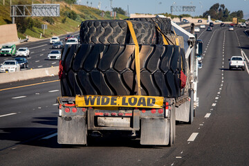 Heavy equipment tires being hauled on a flatbed trailer with a wide load sign