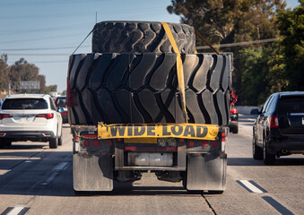 Heavy equipment tires being hauled on a flatbed trailer with a wide load sign