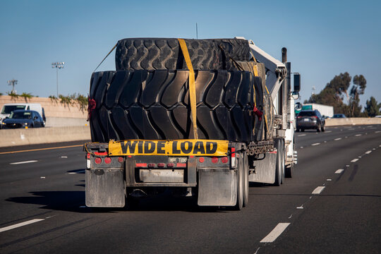Heavy equipment tires being hauled on a flatbed trailer with a wide load sign