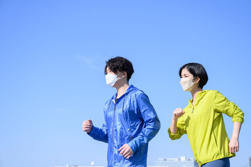 青い空で運動する健康的な男女　マスクつき　横顔